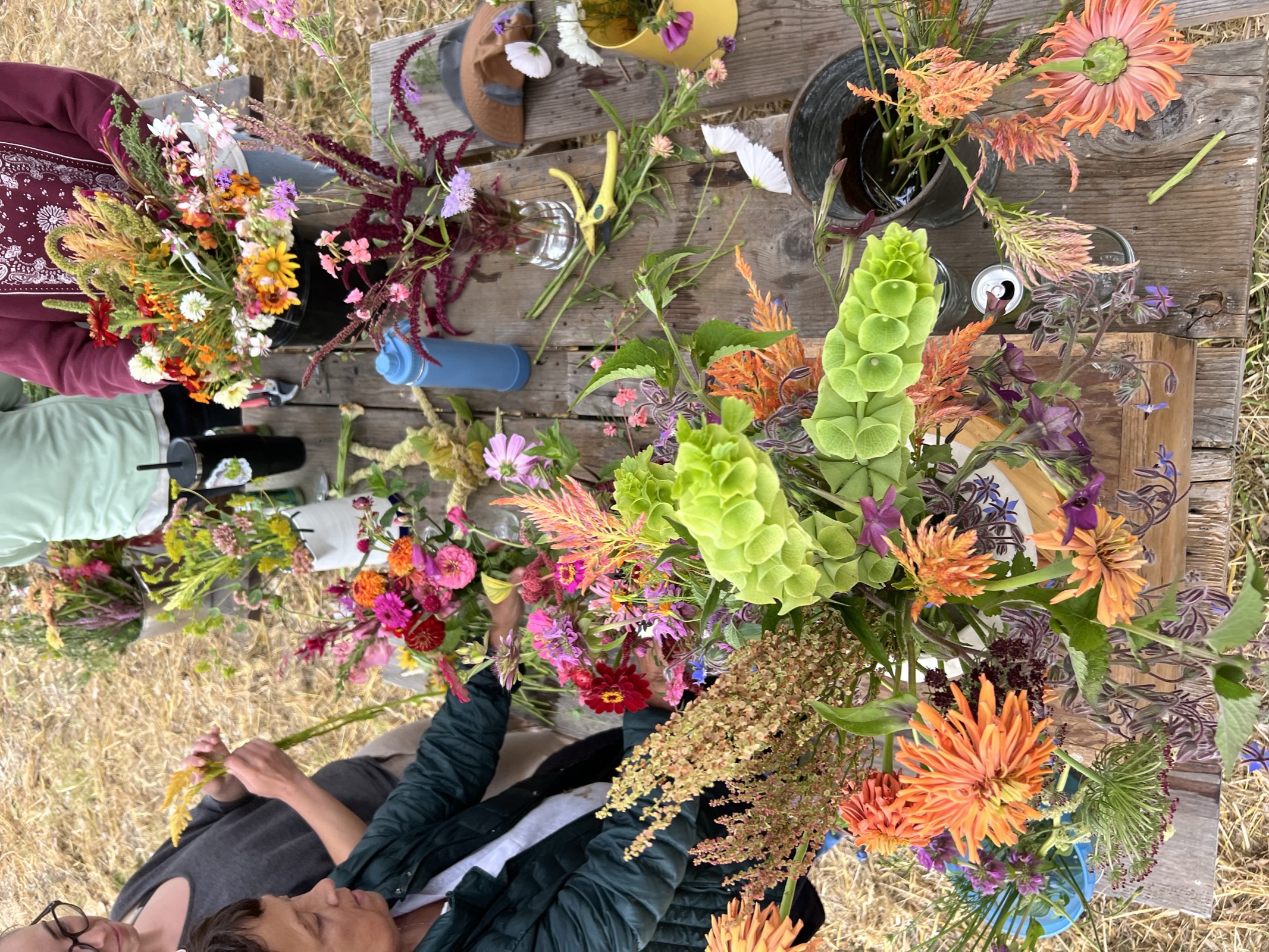 Workshop guests build their own arrangements at a long wooden table covered in just-cut stems and greenery.